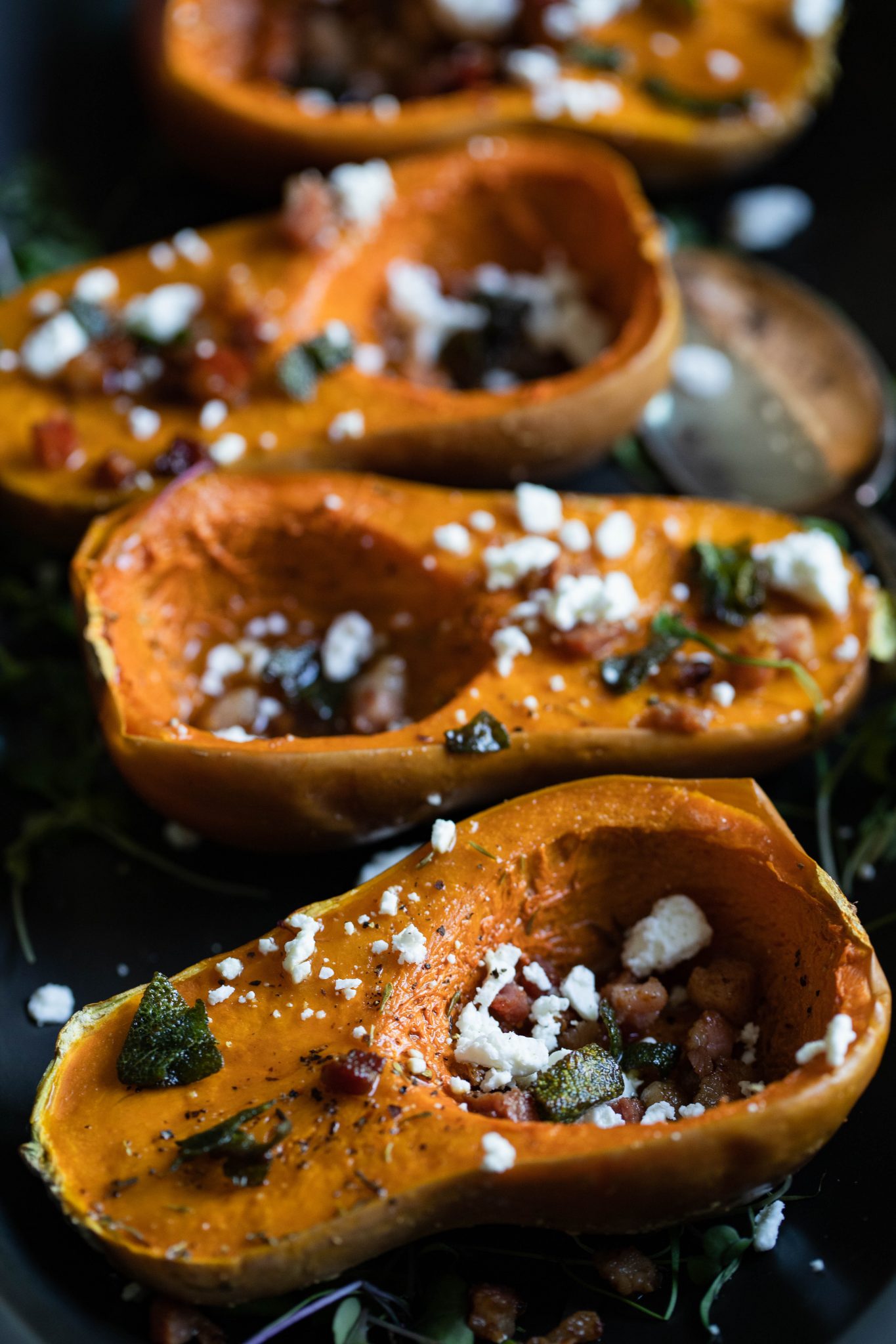 mini squash with pancetta and goat cheese sprinkled on top, assembled on a black platter 