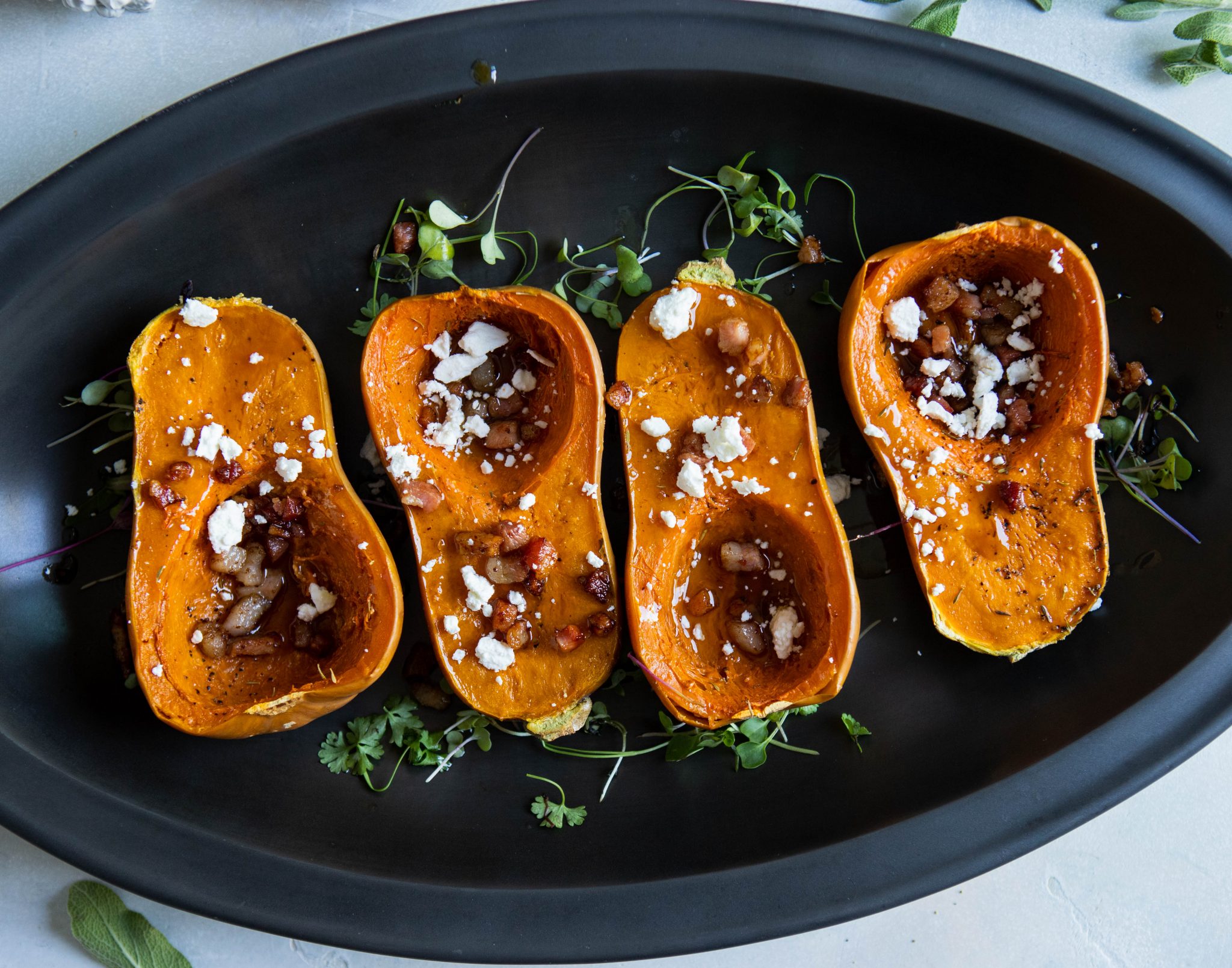 baked squash with pancetta and goat cheese sprinkled on top, in a black serving platter