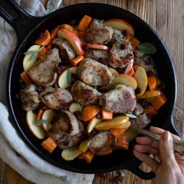 Woman's hand holding a spoon to serve a pork tenderloin dish out of a cast iron skillet
