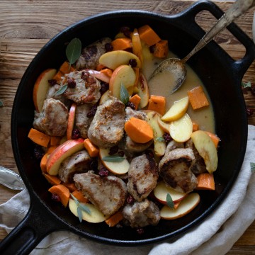 black cast iron skillet with pork tenderloin, apples and sweet potatoes on a wooden board