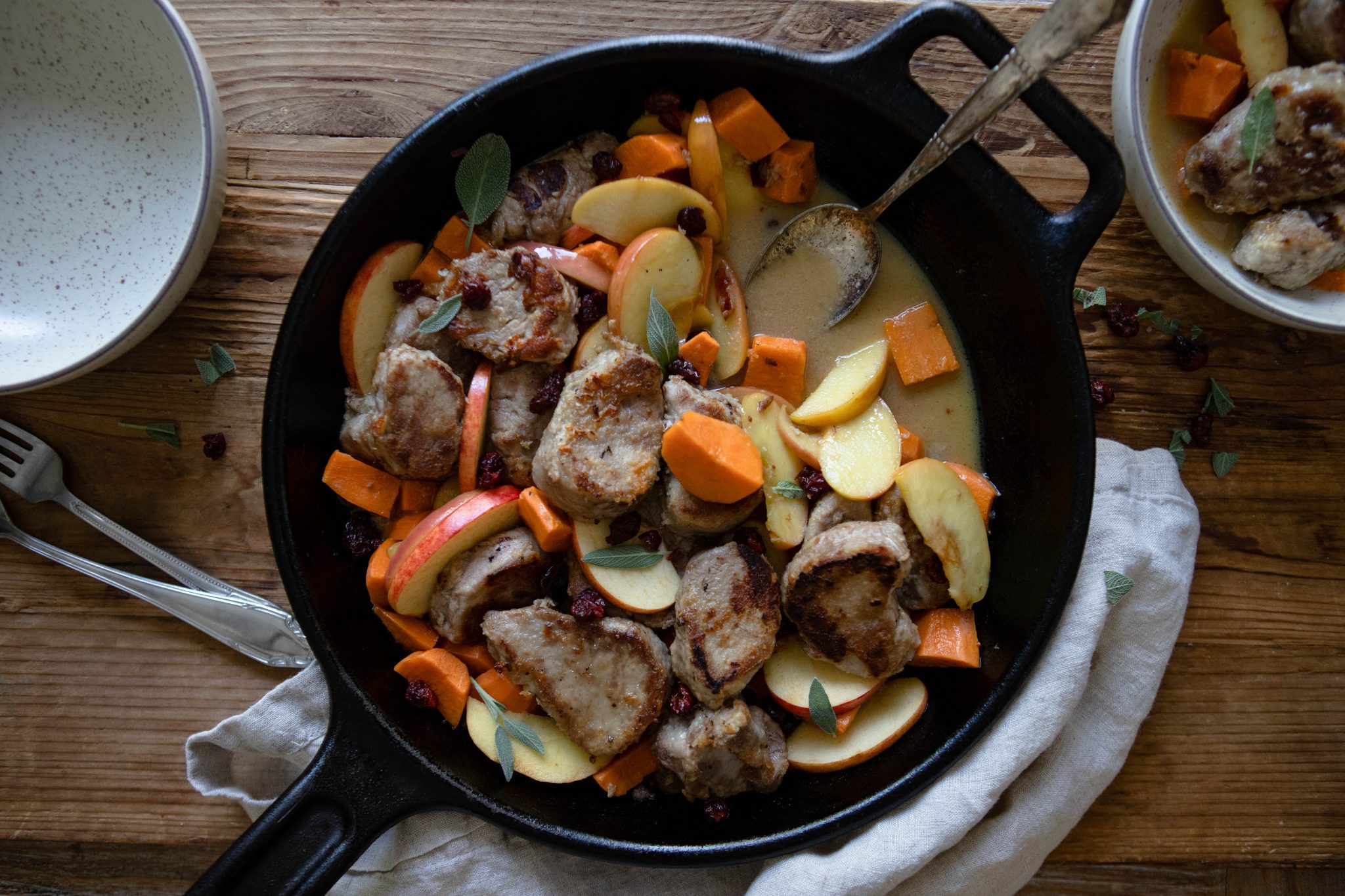 black cast iron skillet with pork tenderloin, apples and sweet potatoes on a wooden board