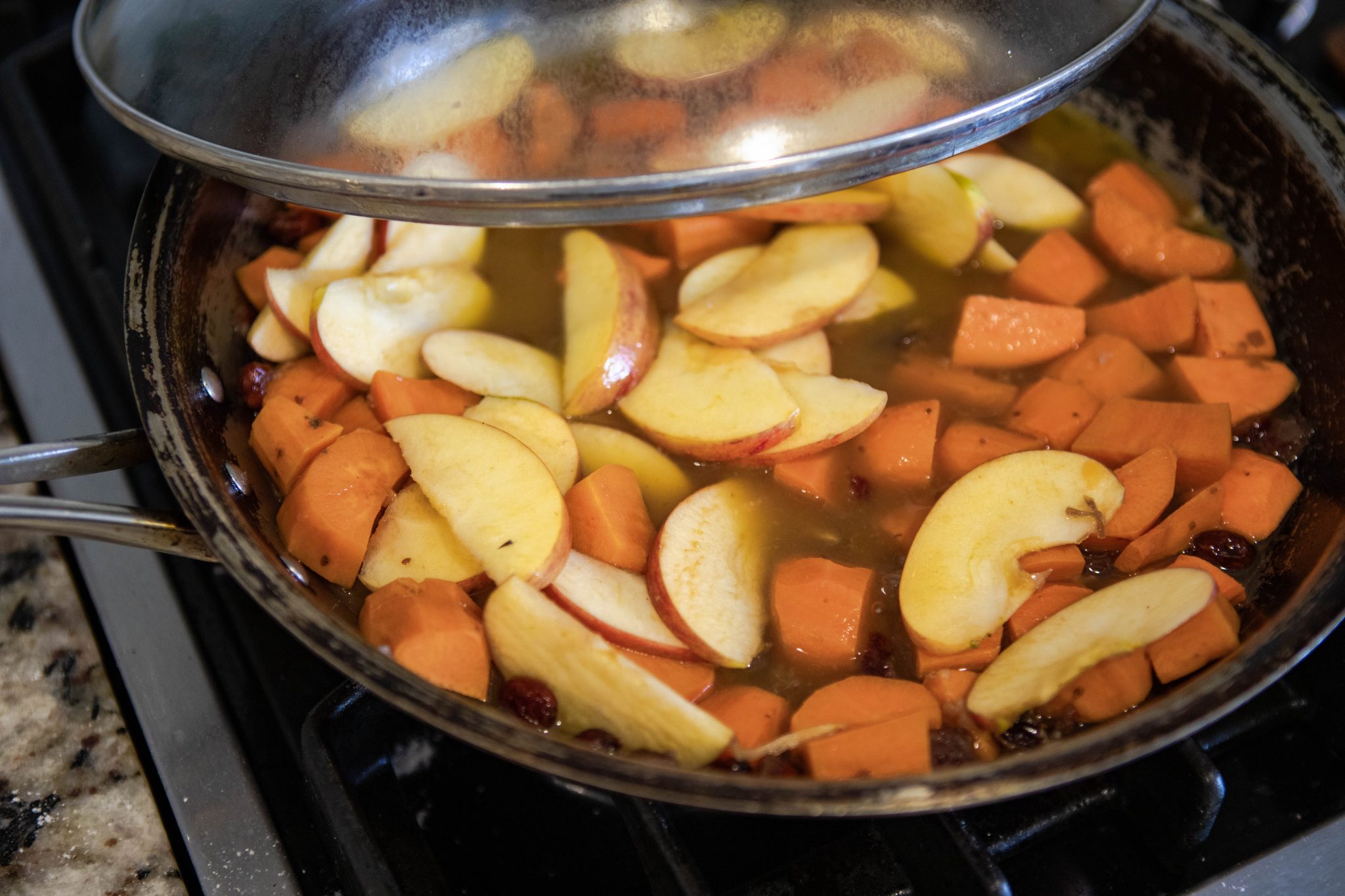 apples, sweet potatoes, and cranberries in skillet with lid being added