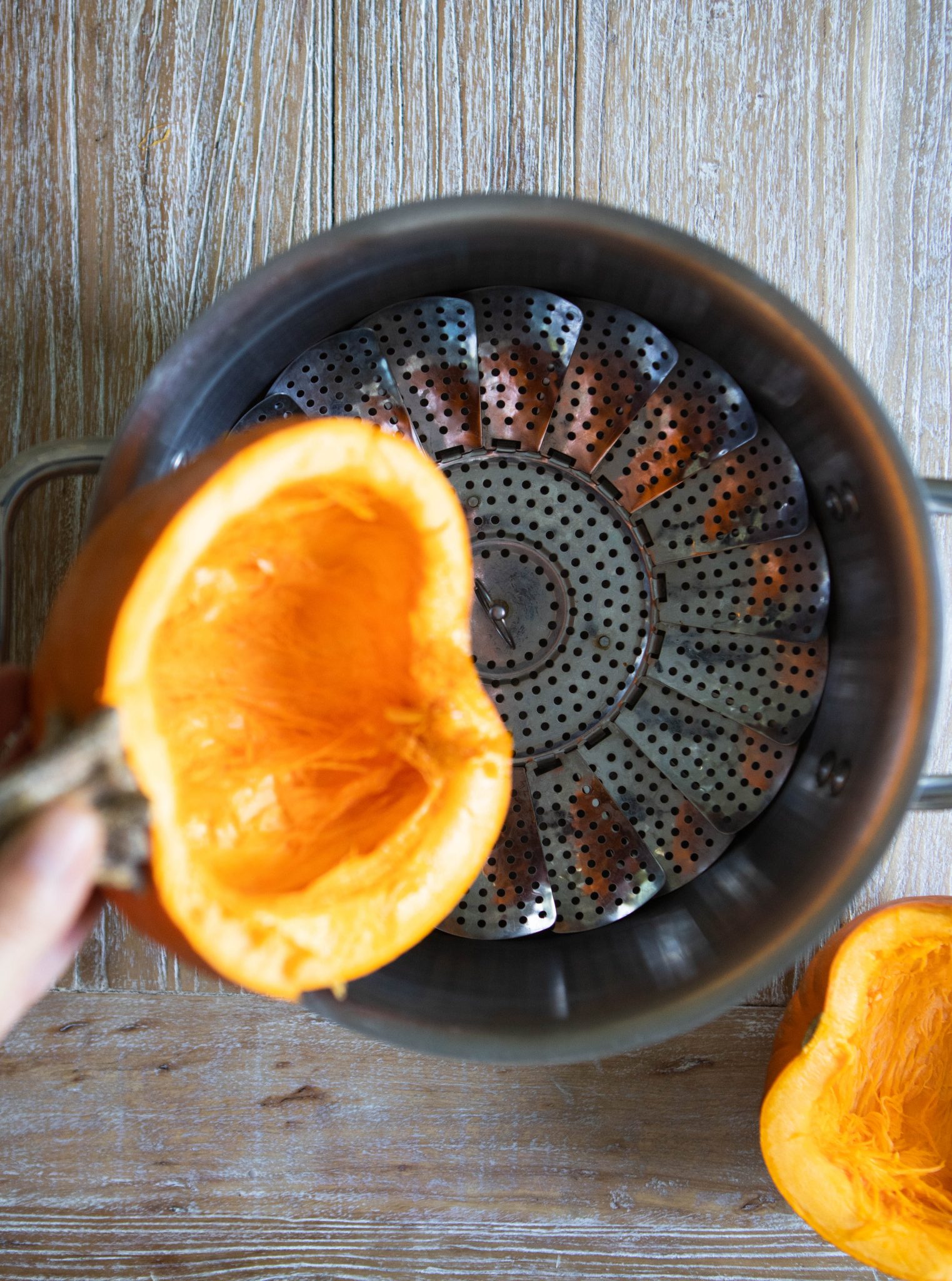 half of a orange pumpkin being placed in a stock pot with a steamer basket insert