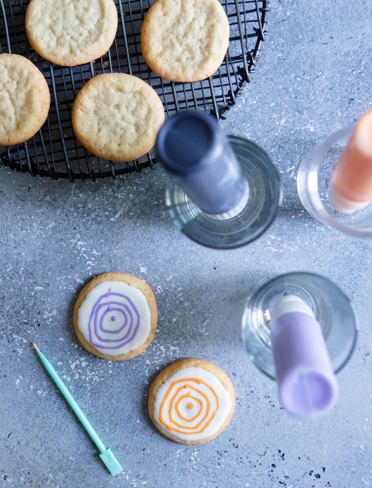colored icing in decorating tubes, upside down in glasses, next to halloween cookies
