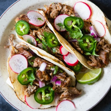 carnitas tacos with garnishes of radish, jalapeno and lime