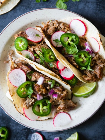 carnitas tacos with garnishes of radish, jalapeno and lime