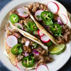 carnitas tacos with garnishes of radish, jalapeno and lime