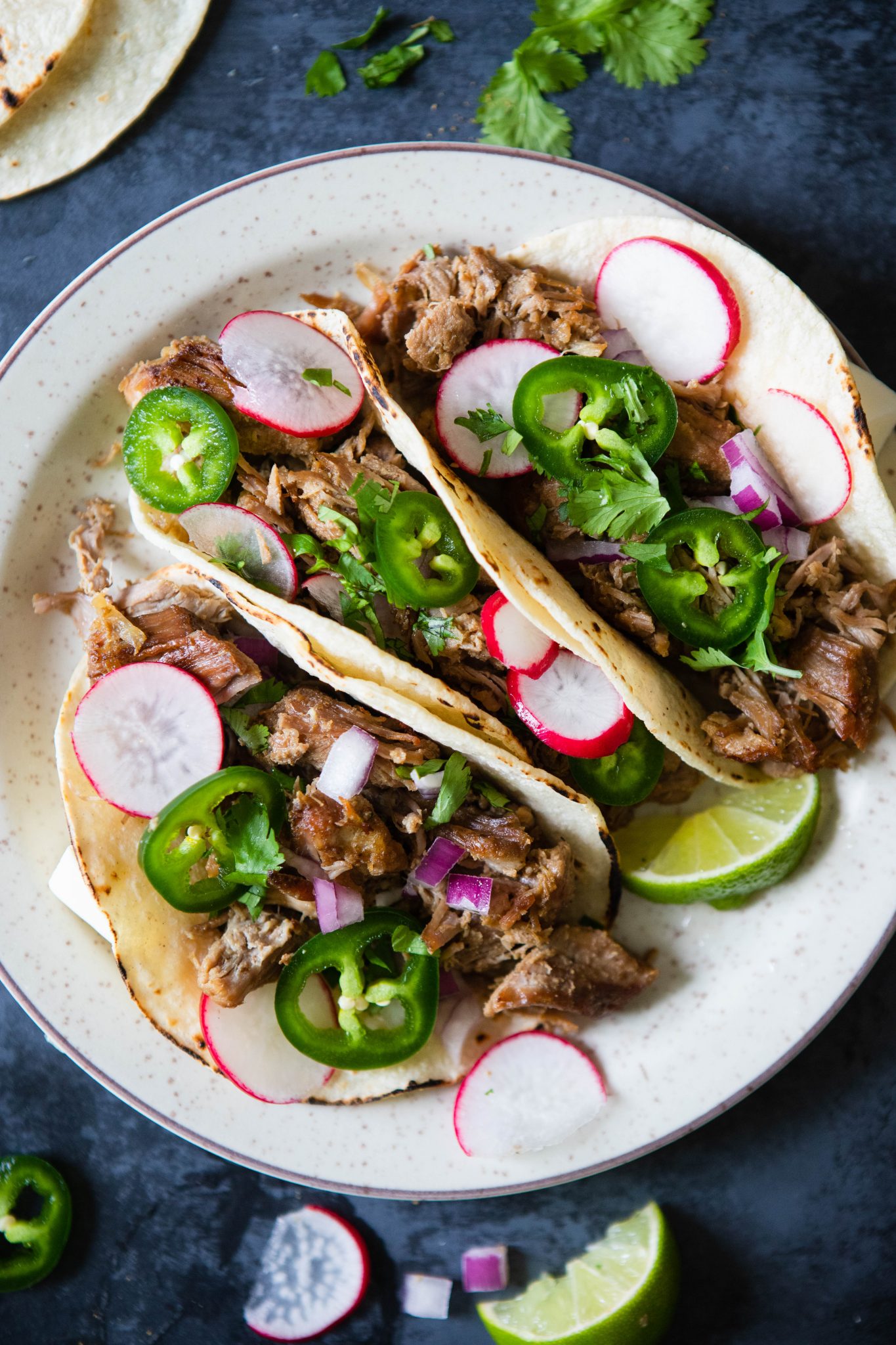 carnitas tacos with garnishes of radish, jalapeno and lime