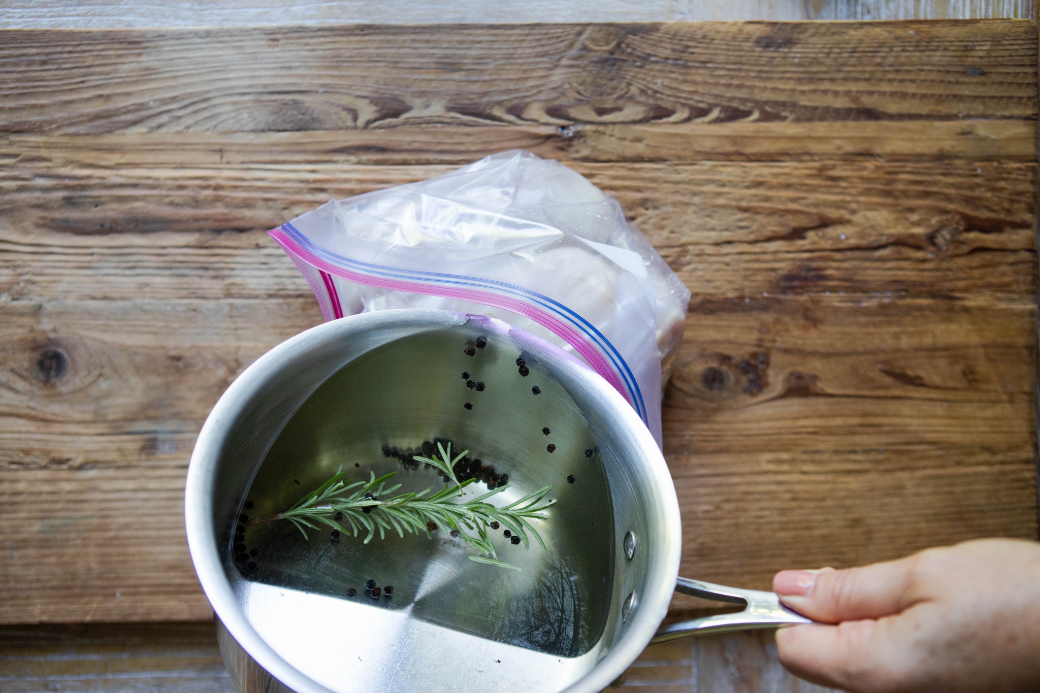 pouring a basic brine with rosemary into a Ziploc bag filled with chicken breasts 