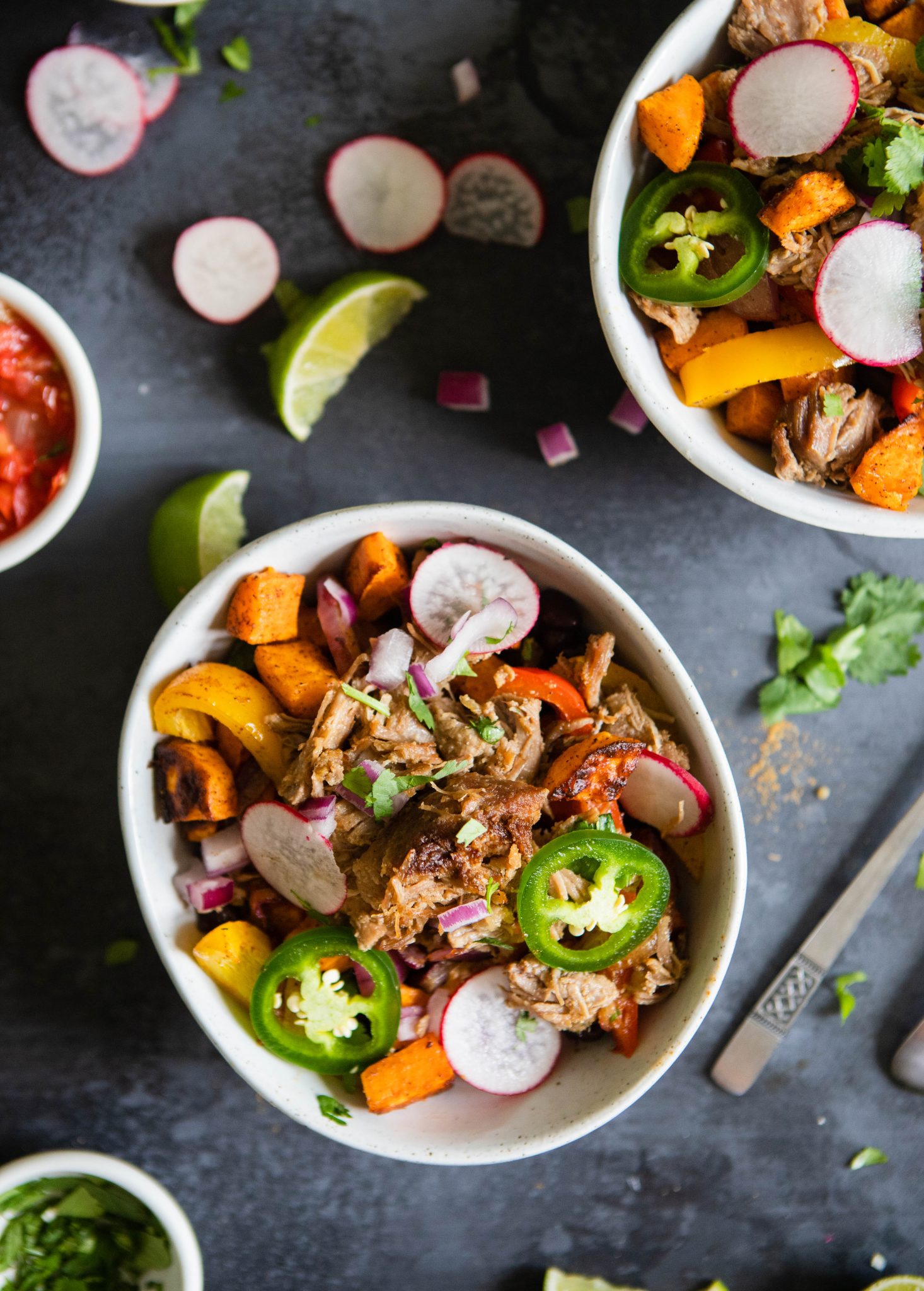 2 bowls filled with carnitas, beans and potatoes and topped with garnishes