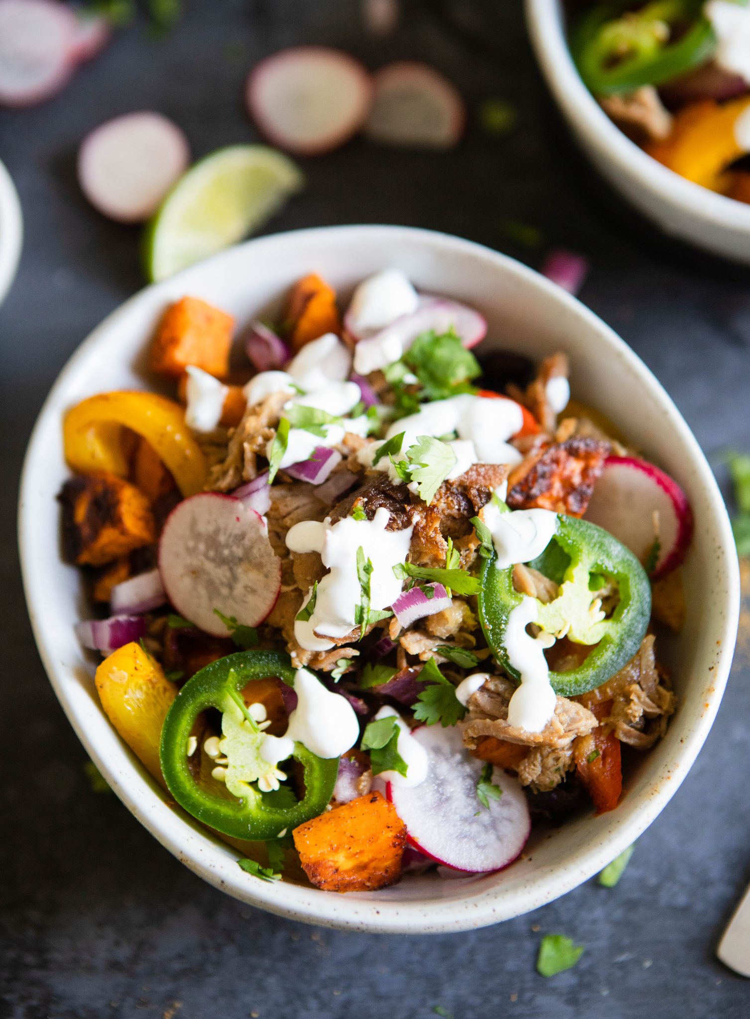 carnitas bowl with jalapeno and radish garnish, in a white bowl