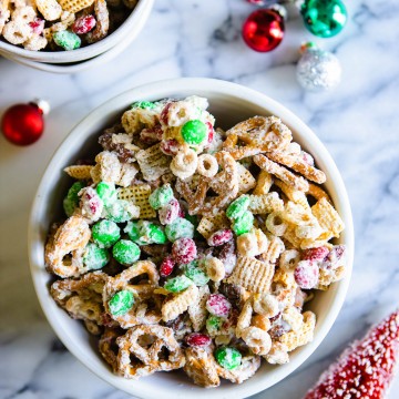 white chocolate, cheerios, rice chex, pretzels and mixed nuts mixed together in a white bowl