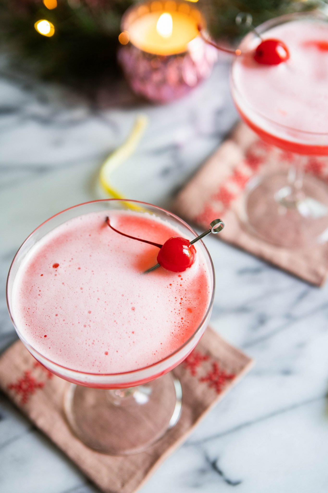 pink cocktail in a coupe glass set against a cocktail napkin and marble backdrop