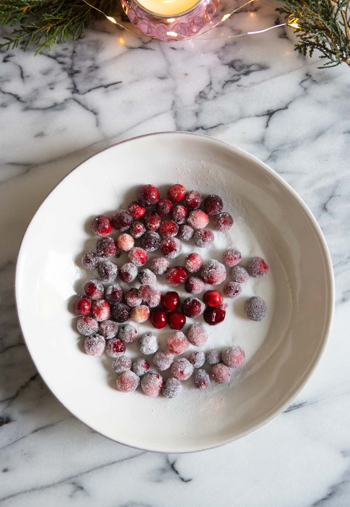 cranberries being tossed in superfine sugar in a white bowl