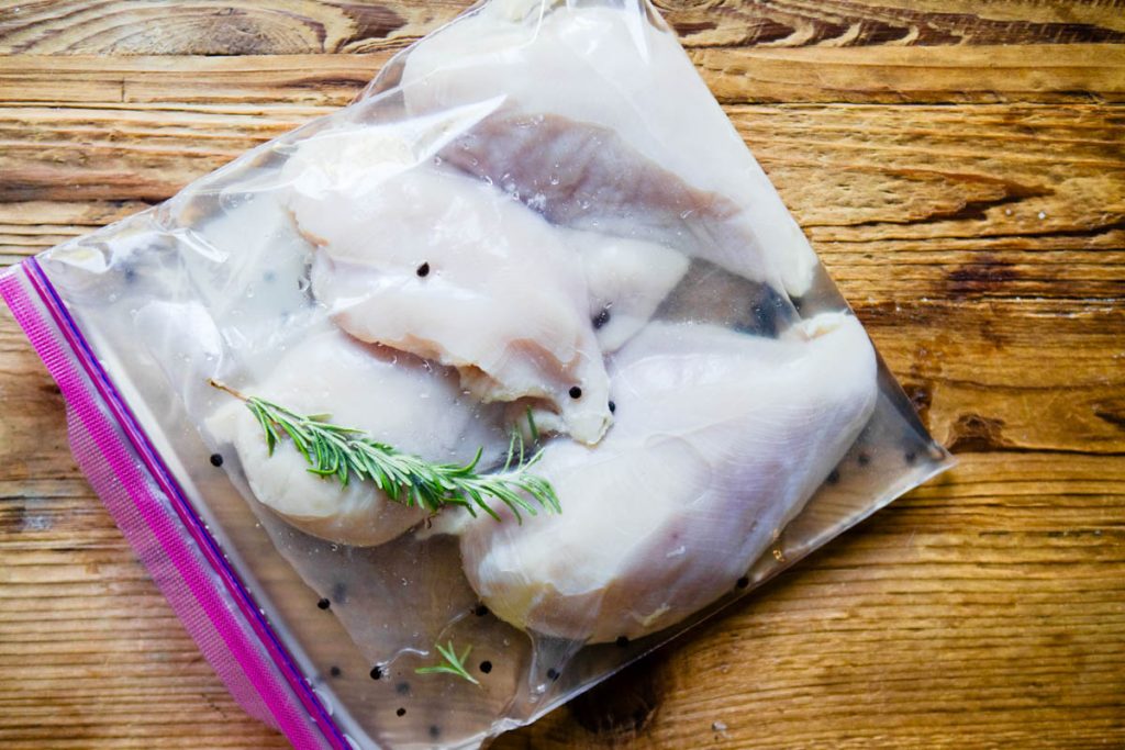 chicken breasts sitting in a salt water brine in a ziploc bag