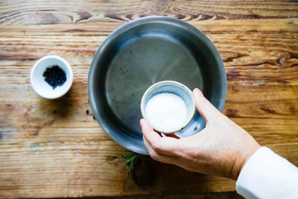 kosher salt being poured into a pan of water to make a brine