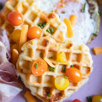 heart shaped waffles topped with tomatoes and chives set on a pink plate