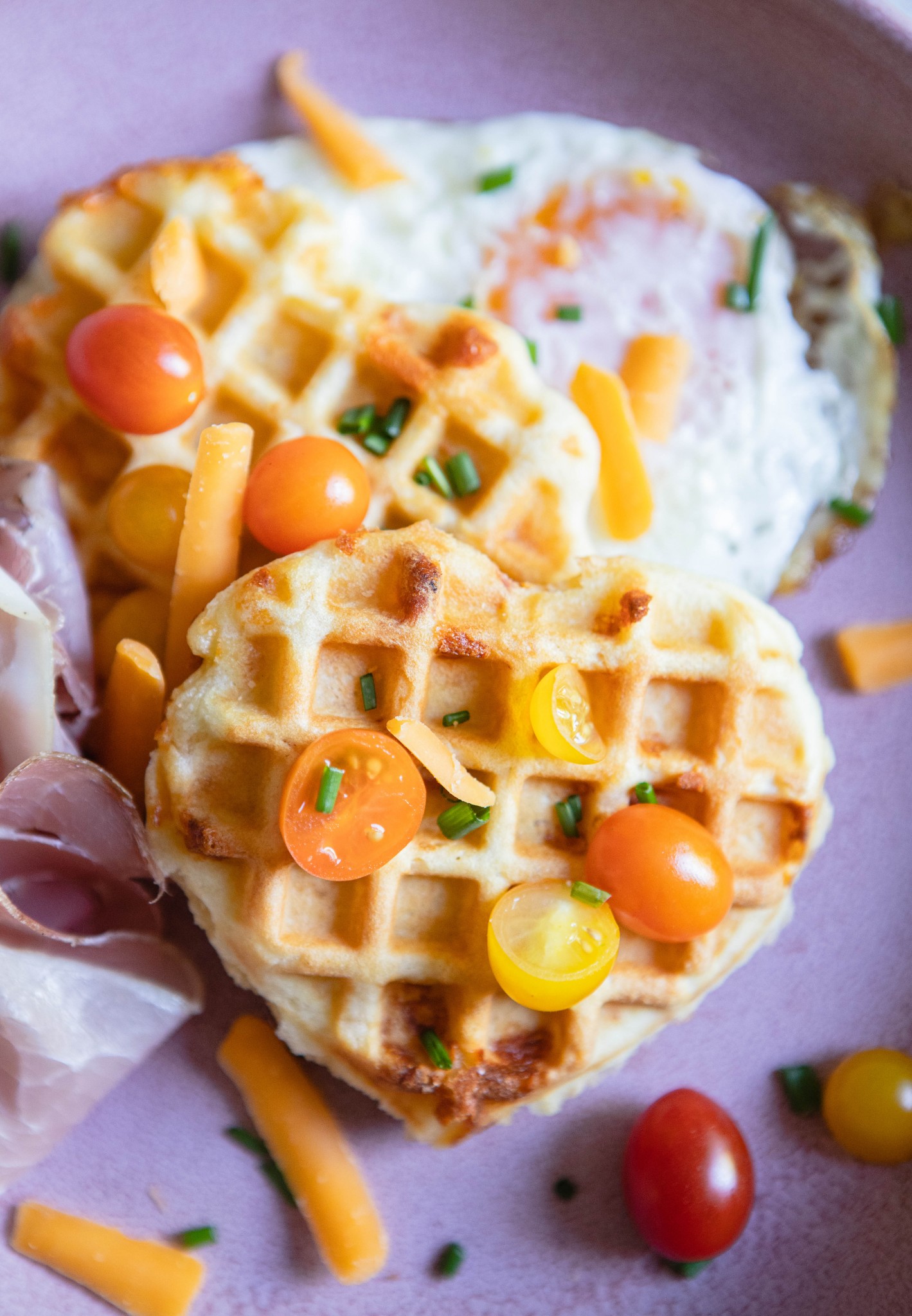 heart shaped waffles topped with tomatoes and chives set on a pink plate