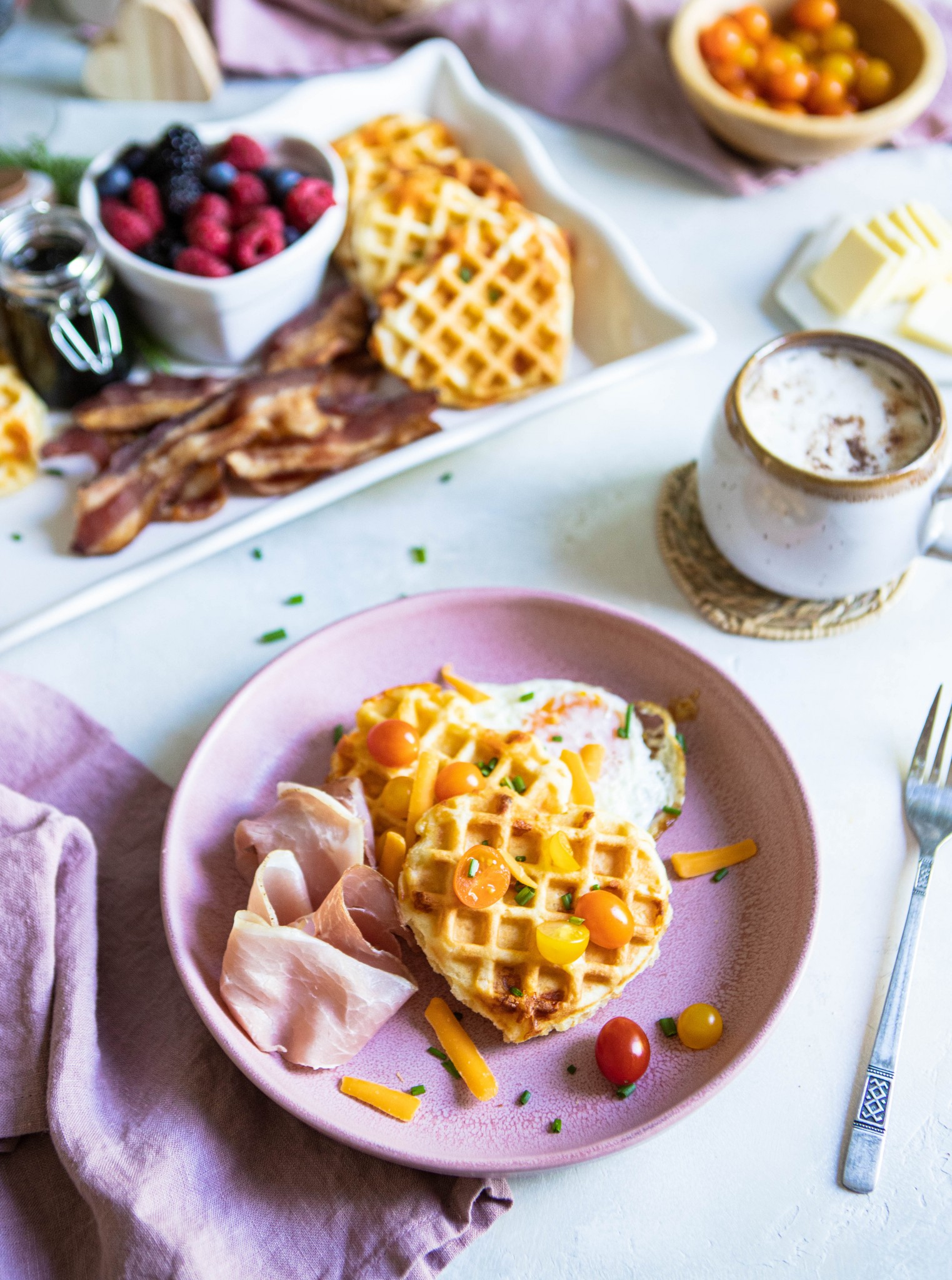 savory waffles on a pink plate next to fruit, and a latte on a white background