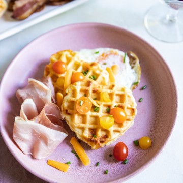 Buttermilk Belgian Waffles on a pink plate topped with tomatoes, cheese and egg