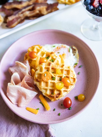 Buttermilk Belgian Waffles on a pink plate topped with tomatoes, cheese and egg