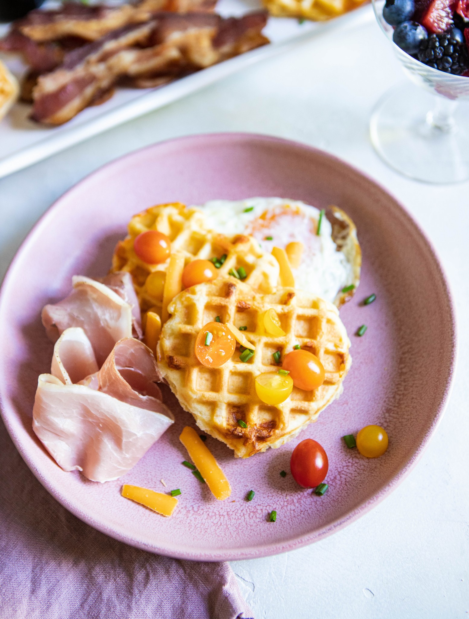 Buttermilk Belgian Waffles on a pink plate topped with tomatoes, cheese and egg