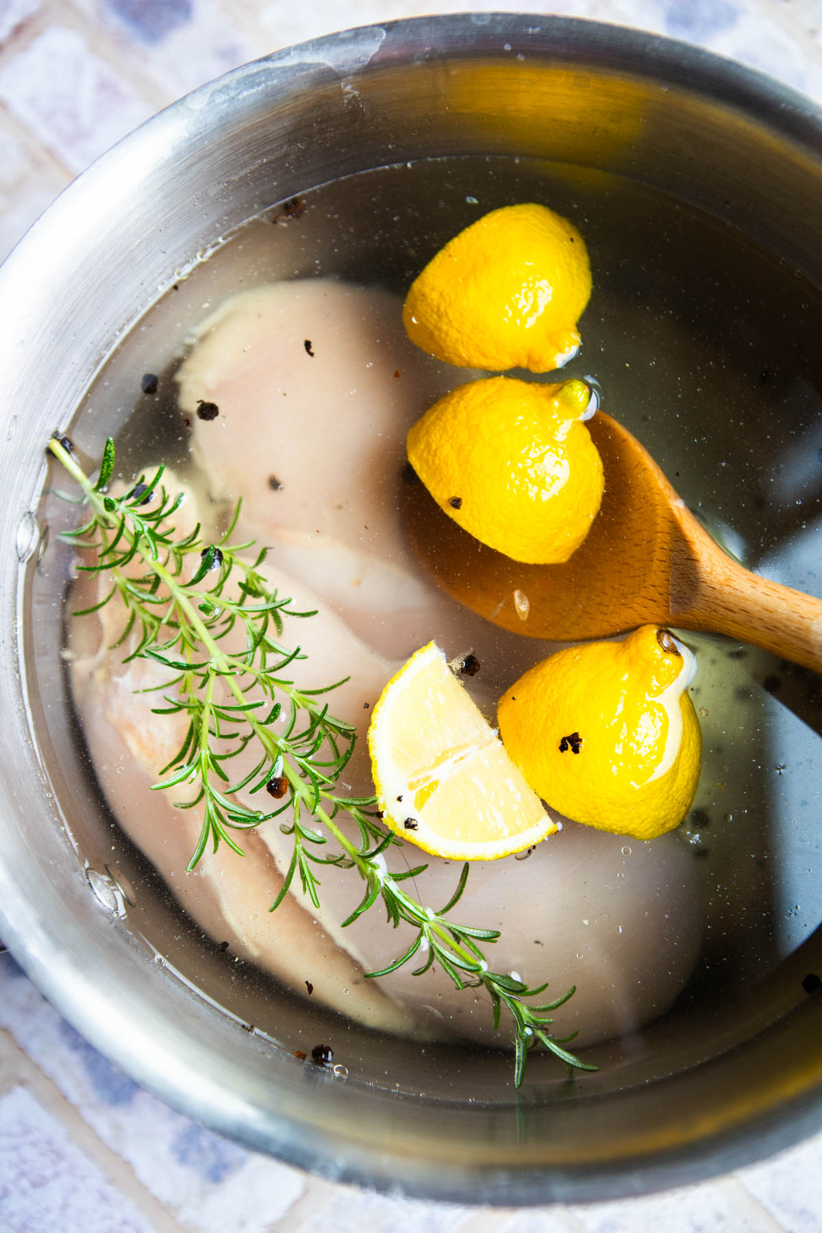 lemon wedges and rosemary in a salt water brine in a stock pot with chicken breasts
