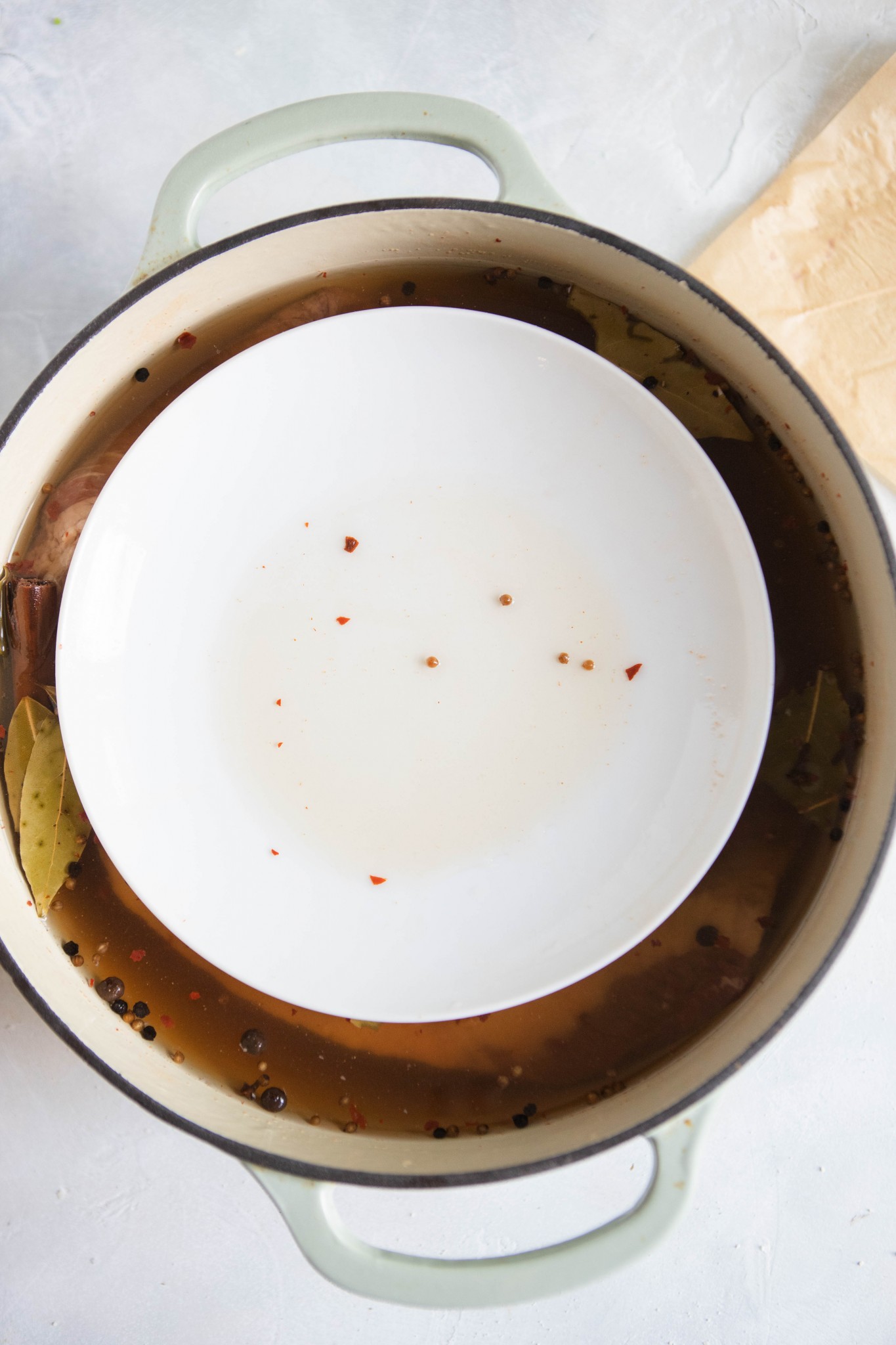 plate set over beef brisket sitting in brine