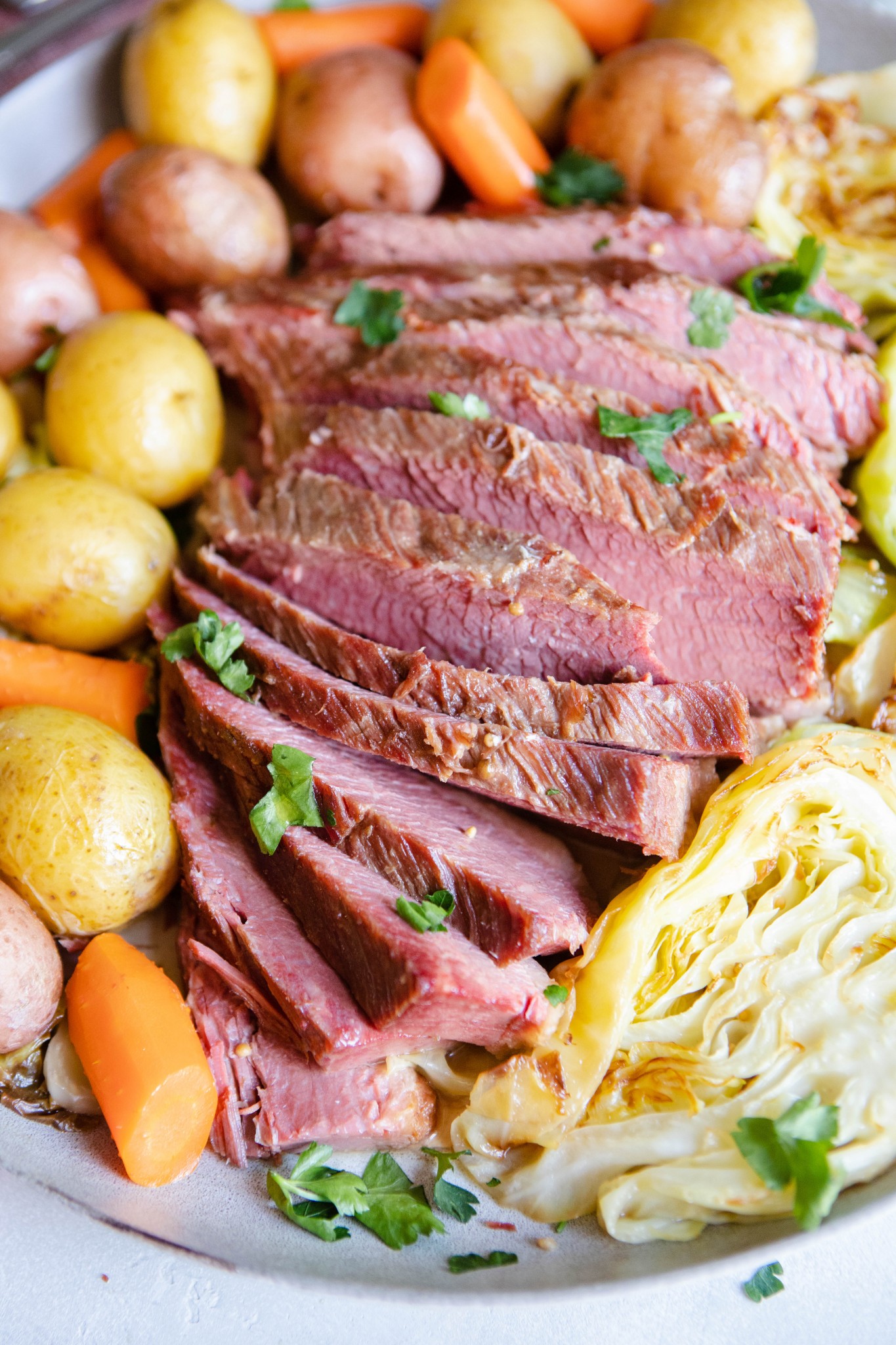 slices of homemade corned beef nestled in between potatoes, carrots and cabbage