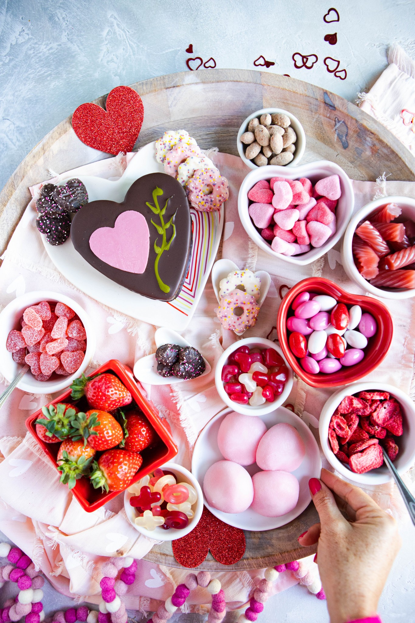 pink mochi ice cream surrounded by other pink and red sweets on a wooden platter