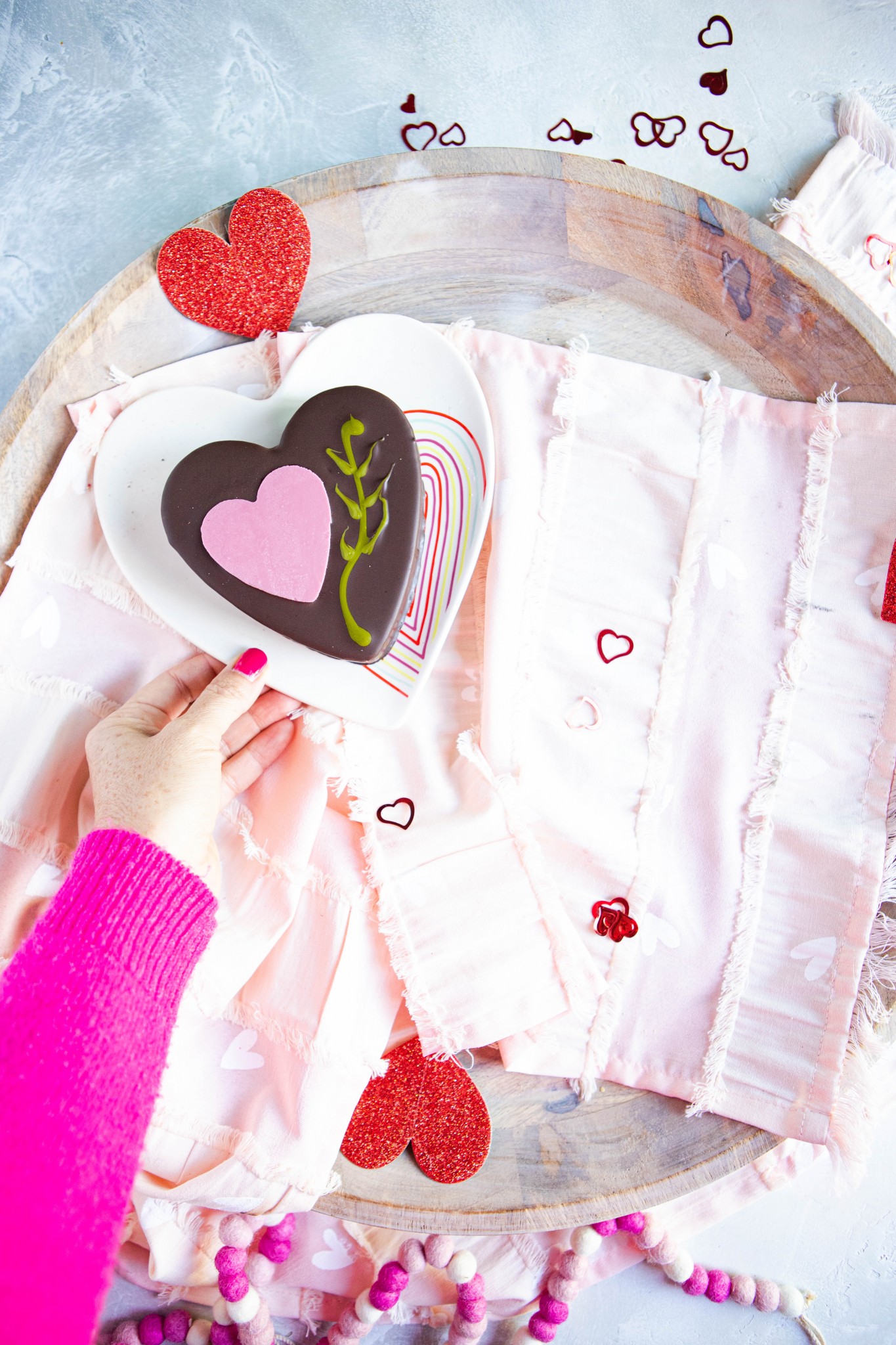 Woman placing a heart chocolate cake on a wooden platter for Valentine's Day