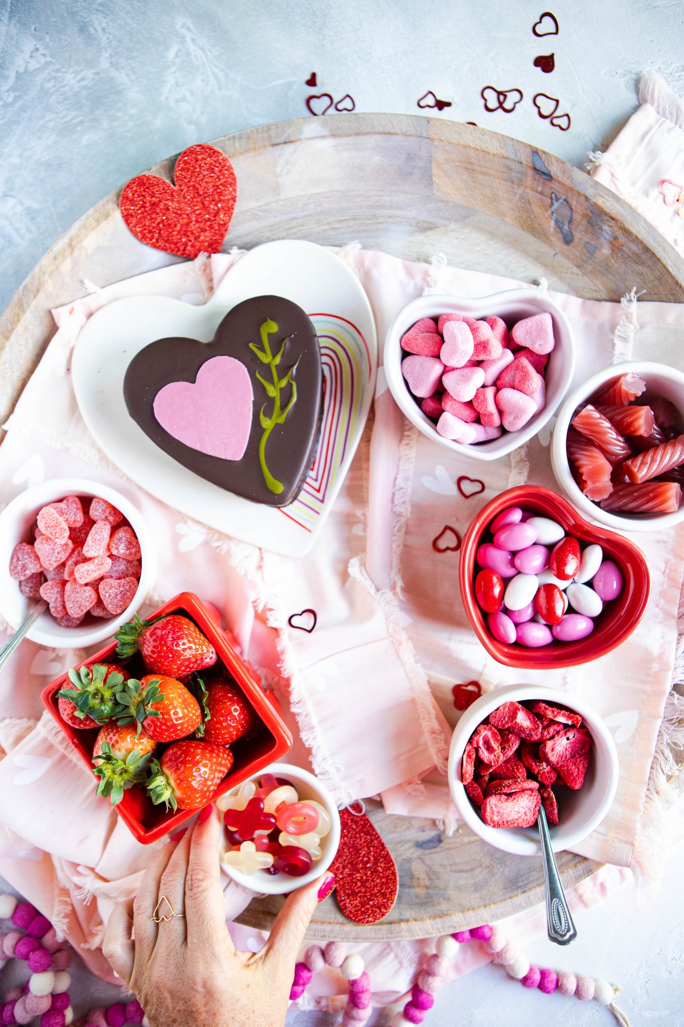 woman's hand placing Valentine's day candy on a wooden tray, surrounded by other sweets