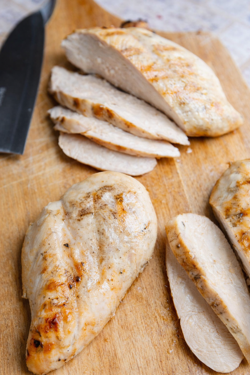 3 chicken breasts on a wood cutting board and sliced thinly