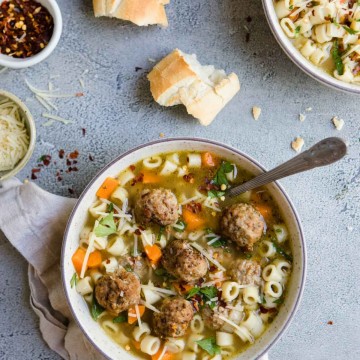 meatball and noodle soup in a beige bowl with garnishes