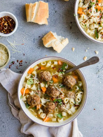 meatball and noodle soup in a beige bowl with garnishes