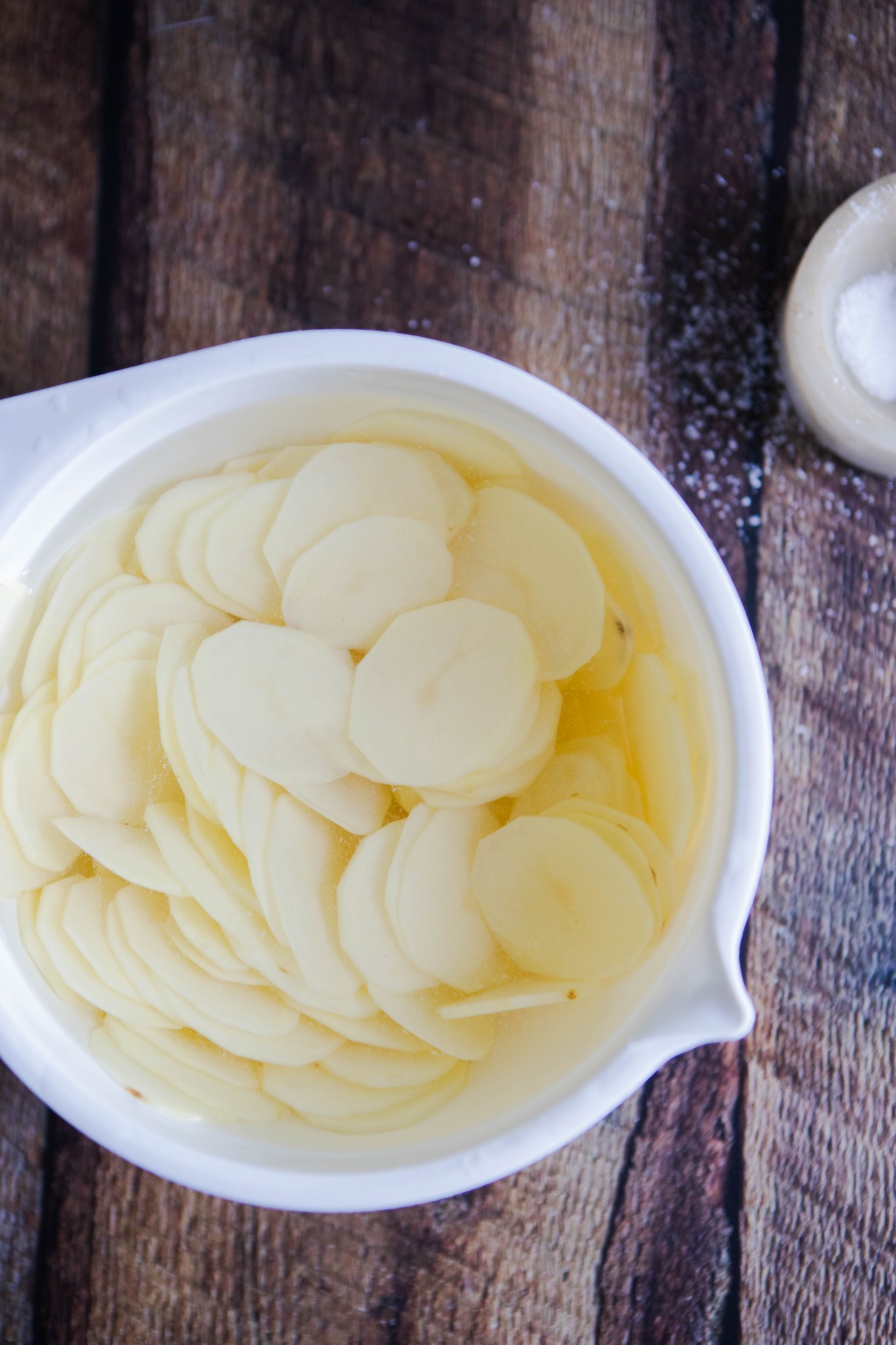 sliced Idaho potatoes soaking in water in a white bowl