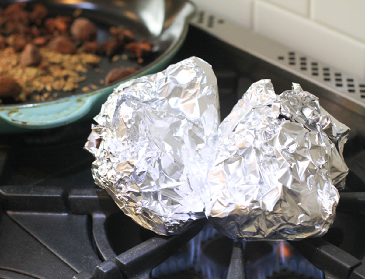 onion and ginger wrapped in tin foil set on an open flame on the stove