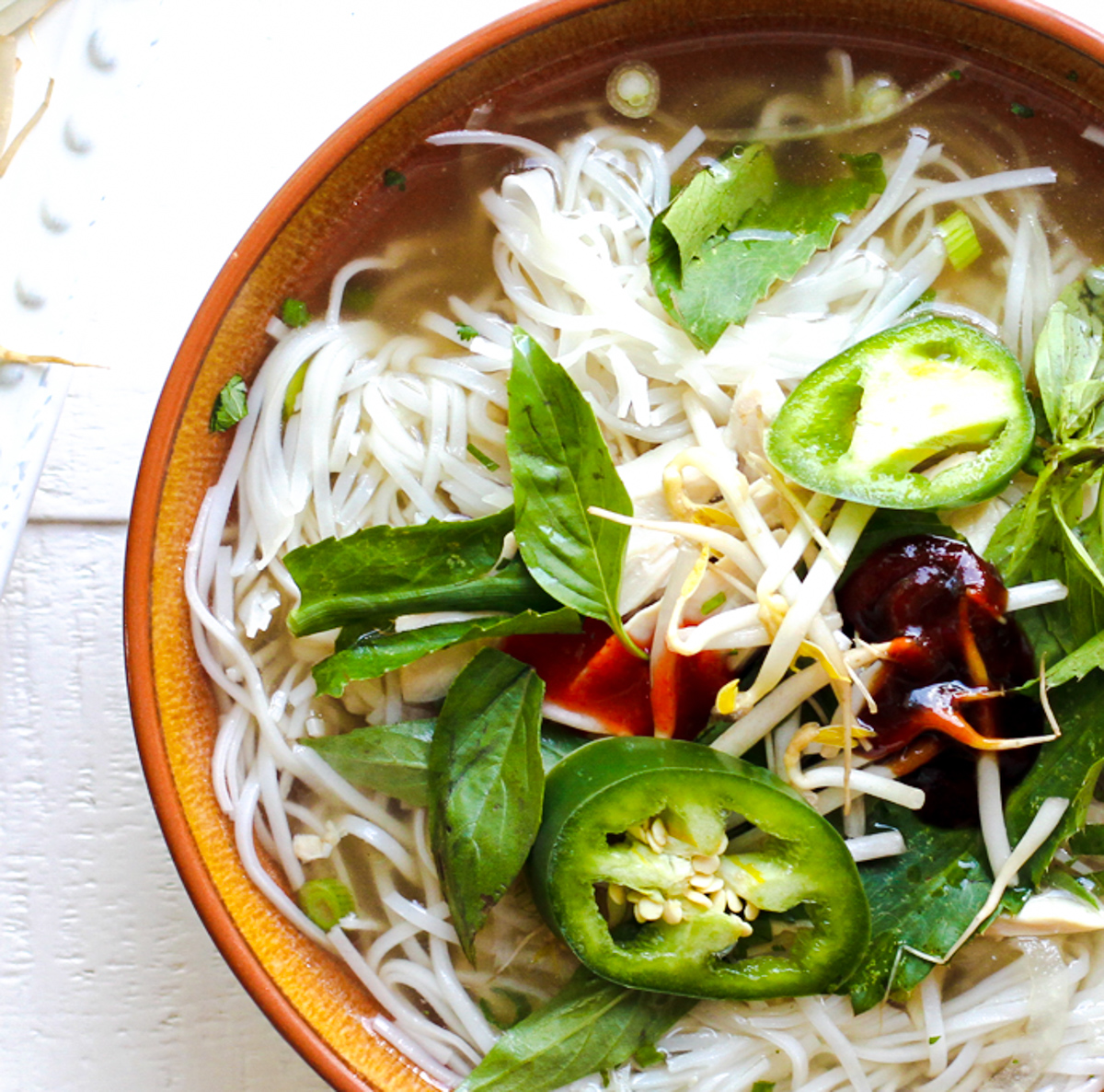 orange bowl filled with chicken pho go noodle soup topped with green garnish