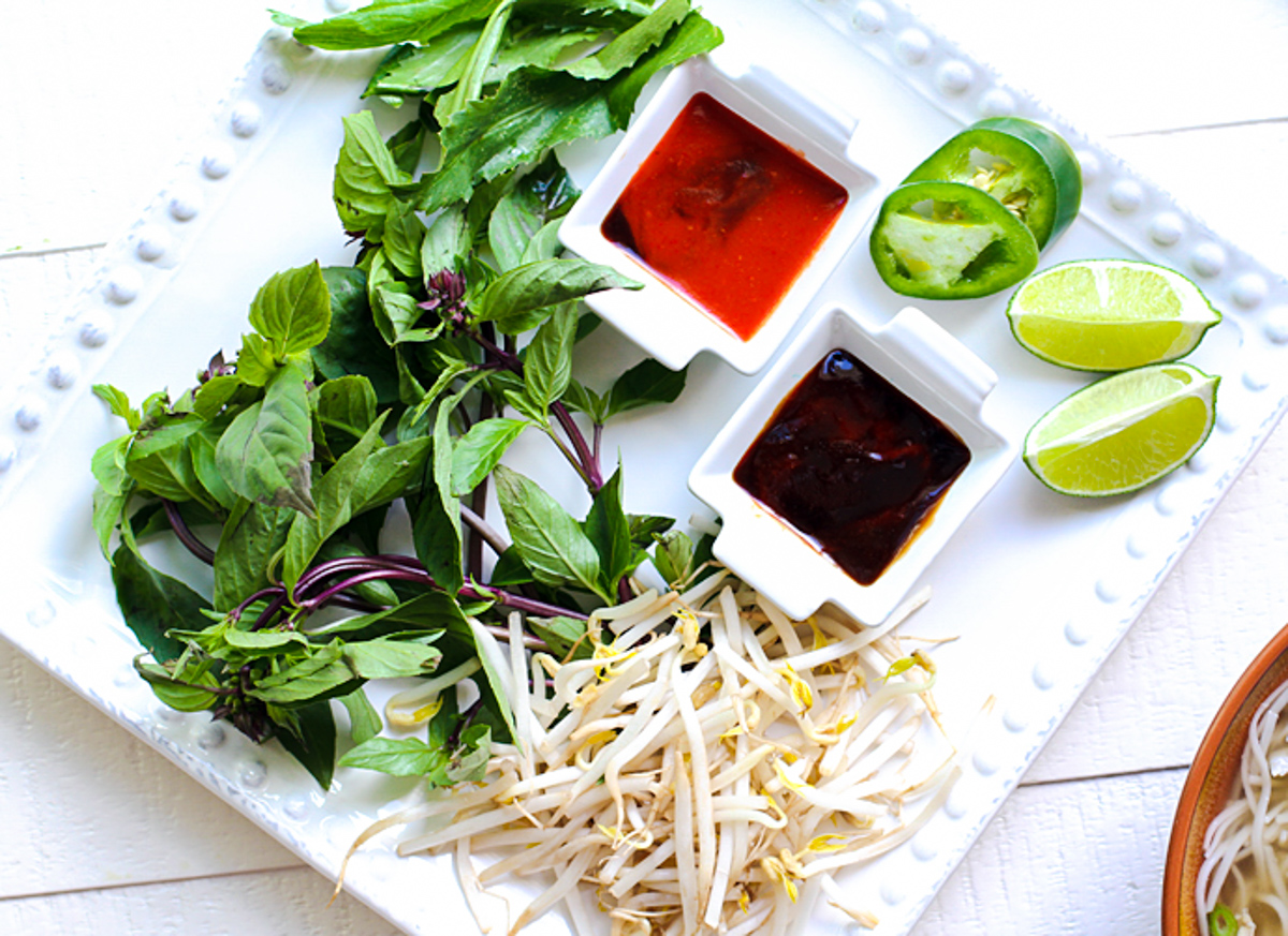 white plate filled with Thai basil, jalapeno, limes, bean sprouts, sriracha and hoisin sauce