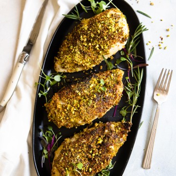 platter of chicken breasts with pistachio crust on a black platter and greens
