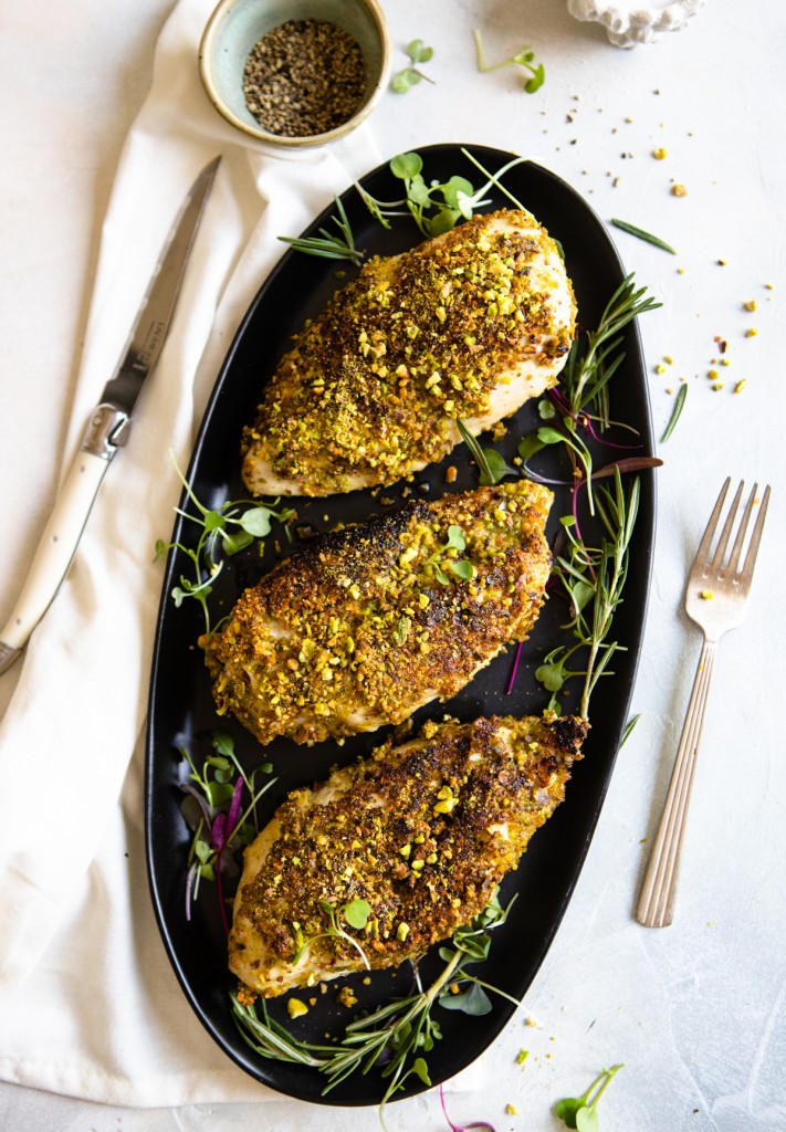 platter of chicken breasts with pistachio crust on a black platter and greens