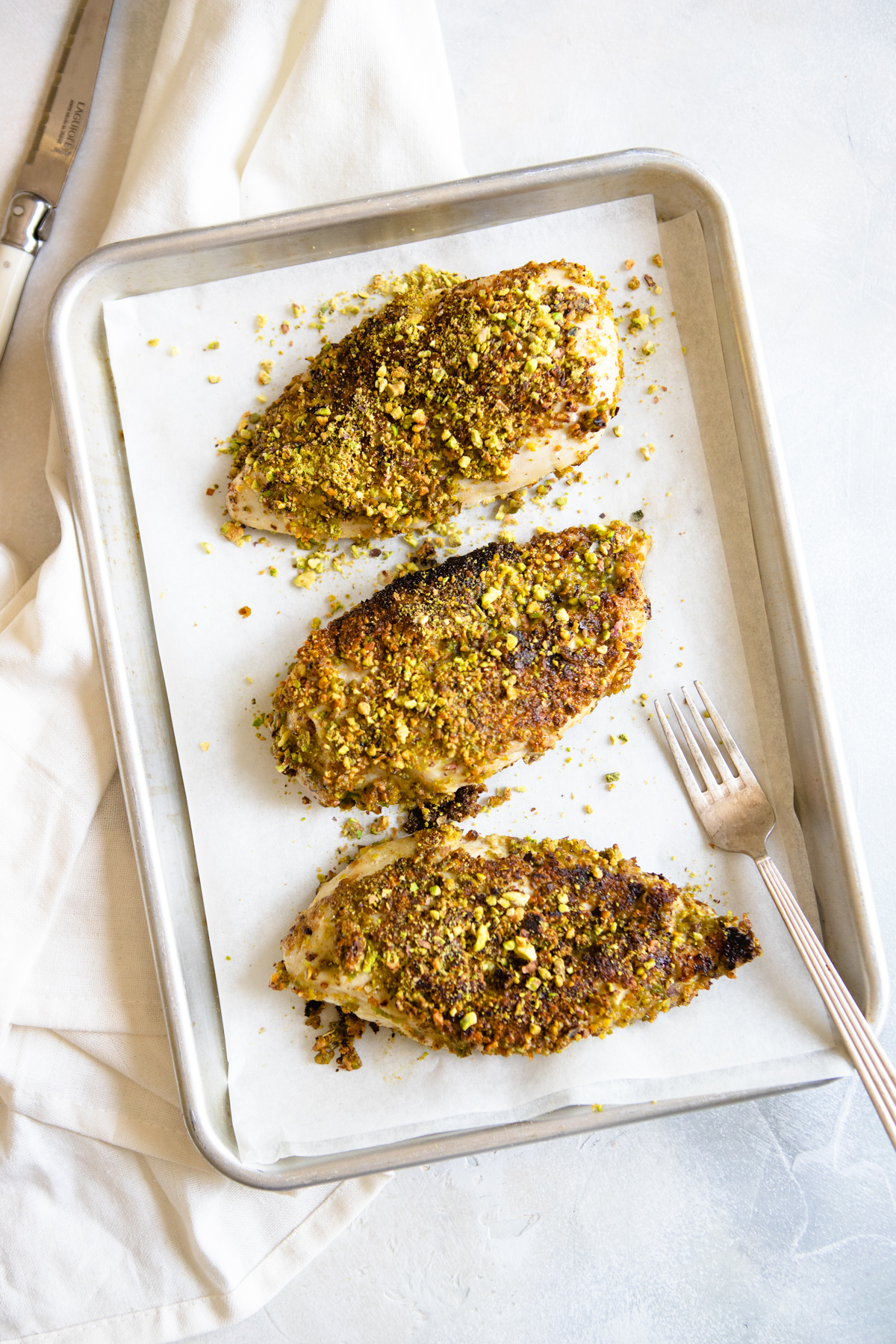 3 baked chicken breasts with pistachio topping placed on a baking sheet