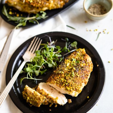 sliced chicken breast on a black plate with a fork and micro greens