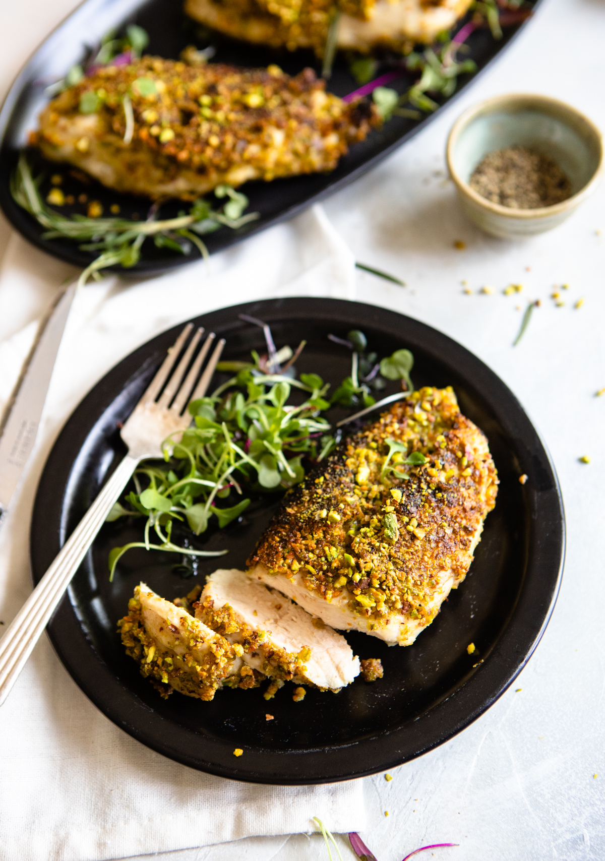 sliced chicken breast on a black plate with a fork and micro greens 