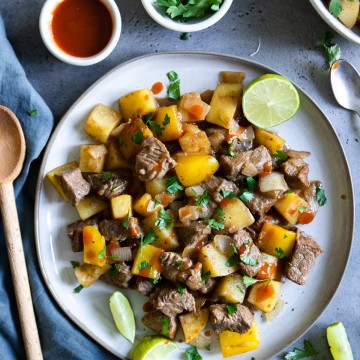 gray plate filled with marinated beef tips, potatoes and bell peppers set atop a gray background