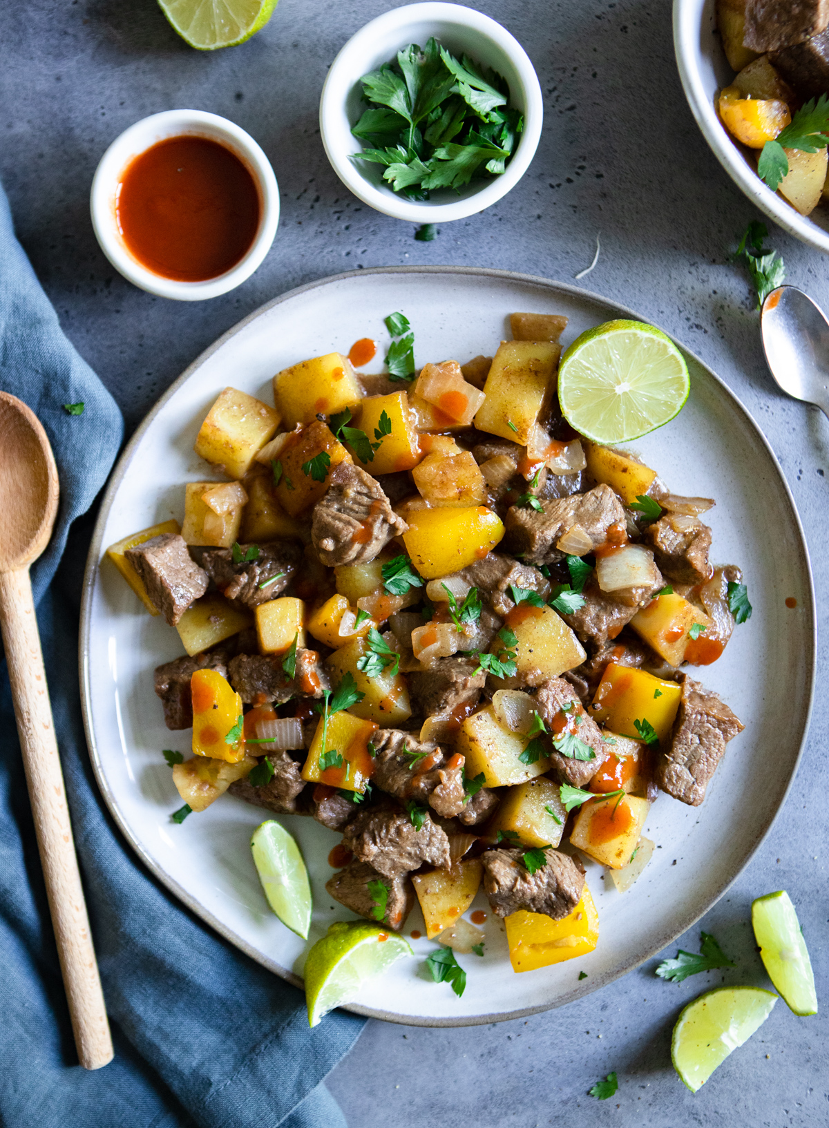 ceramic plate filled with a marinated beef tips and potato dish, with hot sauce sprinkled on top