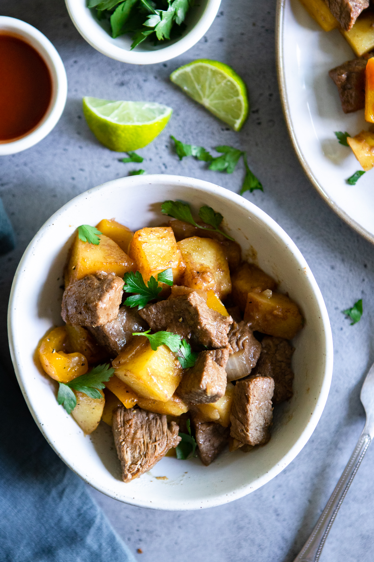 a small bowl filled with marinated beef tips, potatoes and peppers. Garnished with lime.