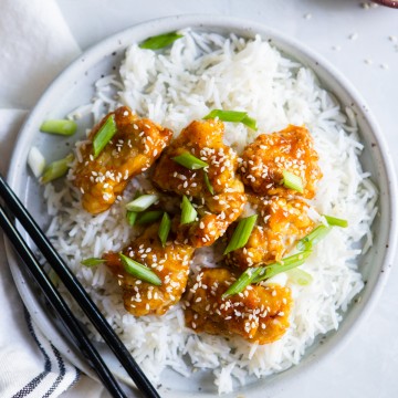 white plate with copycat Trader Joe's orange chicken made in air fryer on a bed of rice with scallions and sesame seeds