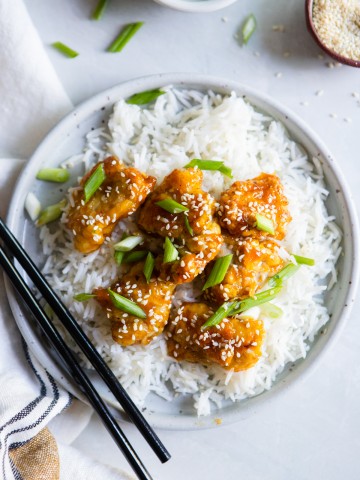 white plate with copycat Trader Joe's orange chicken made in air fryer on a bed of rice with scallions and sesame seeds