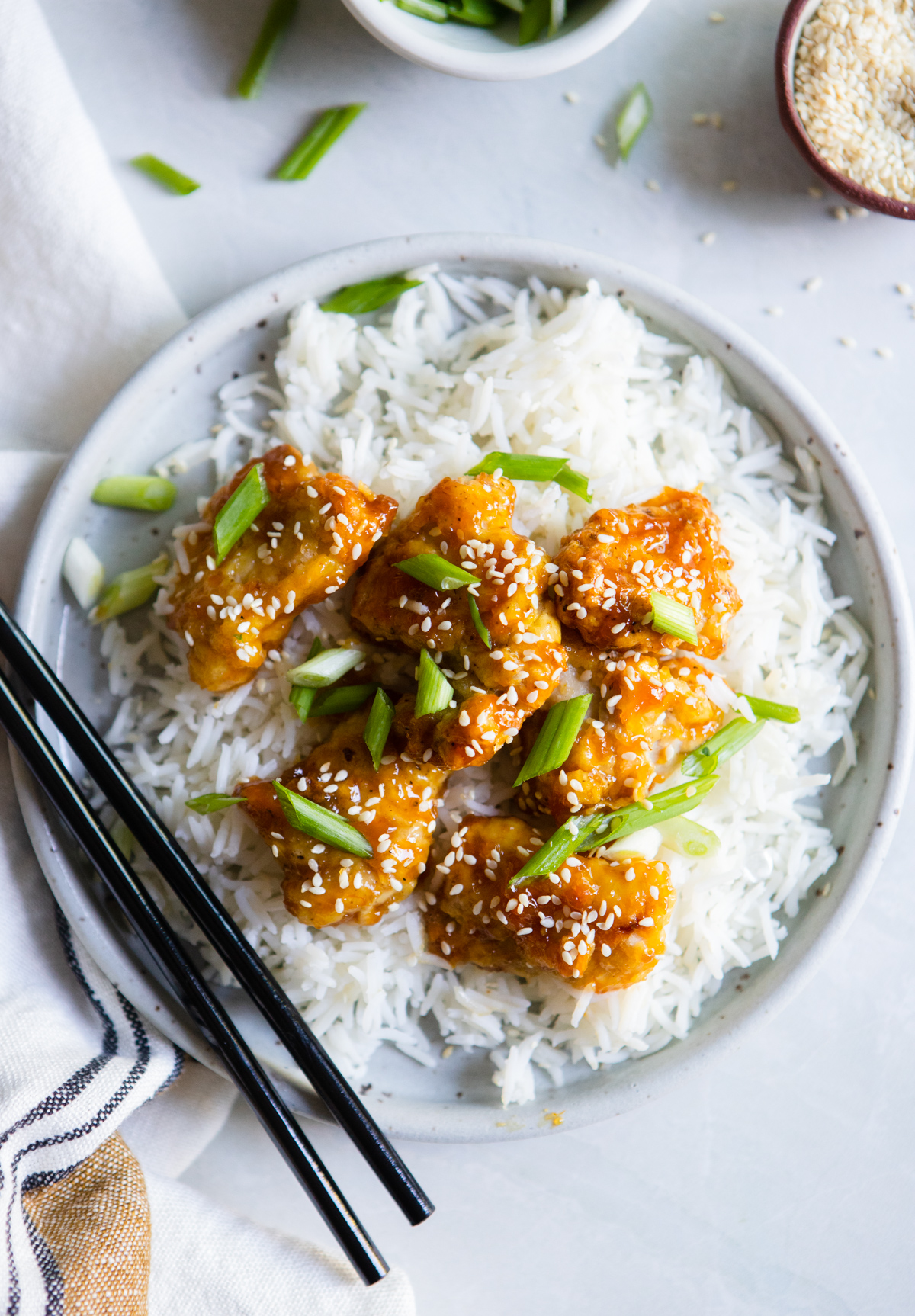 white plate with copycat Trader Joe's orange chicken made in air fryer on a bed of rice with scallions and sesame seeds